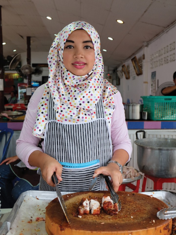 A young Muslim woman cuts up fried chicken at Gai Tod Decha