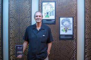 New
Zealand Author, Alastair Carthew, with his new book Proud
and caricature portraits of iconic New Zealander’s in the
background